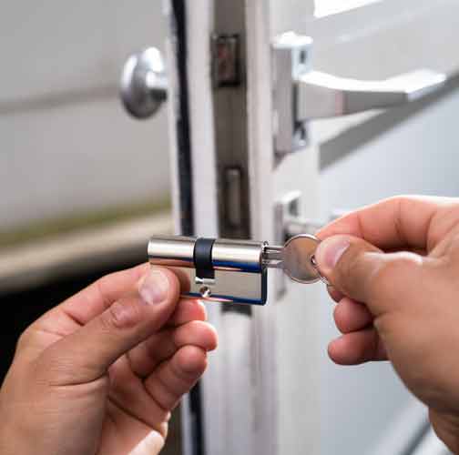 Locksmith holding a lock with a key inserted into it in the foreground. An open UPVC domestic door is in the background. Represents Domestic Locksmith.