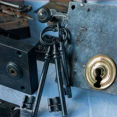 Large door lock with a brass keyhole and three keys on a table with other parts of locks. Represent locksmith fixing locks.